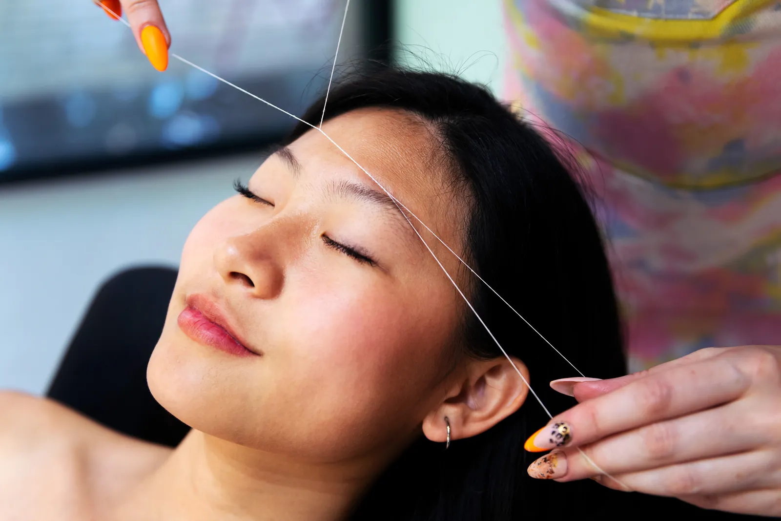 Beautician threading a woman's eyebrows in a salon