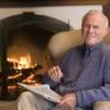 Man relaxing in an armchair by a lit fireplace