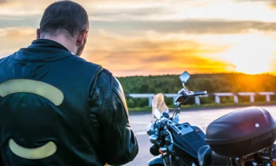 Rider in a leather motorcycle jacket with reflective panels beside his bike at sunset