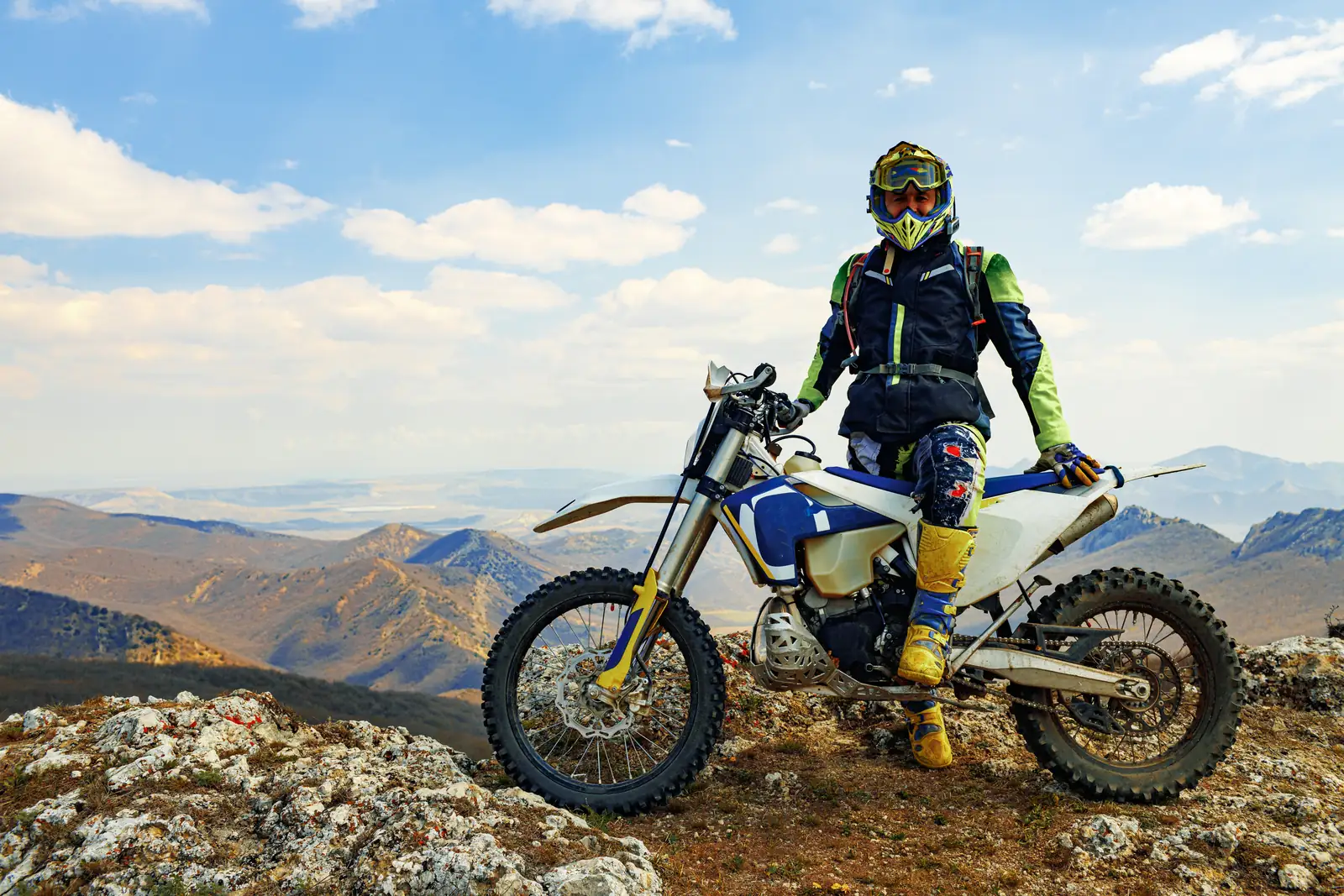 Rider in off-road kit and tall protective boots beside a trail bike