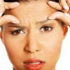 Woman stretching her forehead skin to check for wrinkles