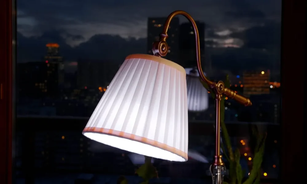 Table lamp with a pleated shade glowing by a window on a dark evening