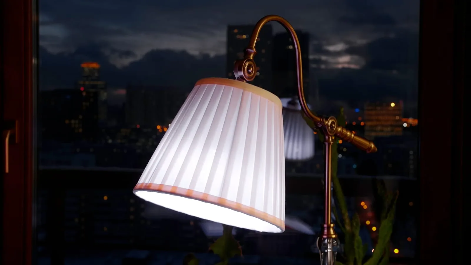 Table lamp with a pleated shade glowing by a window on a dark evening